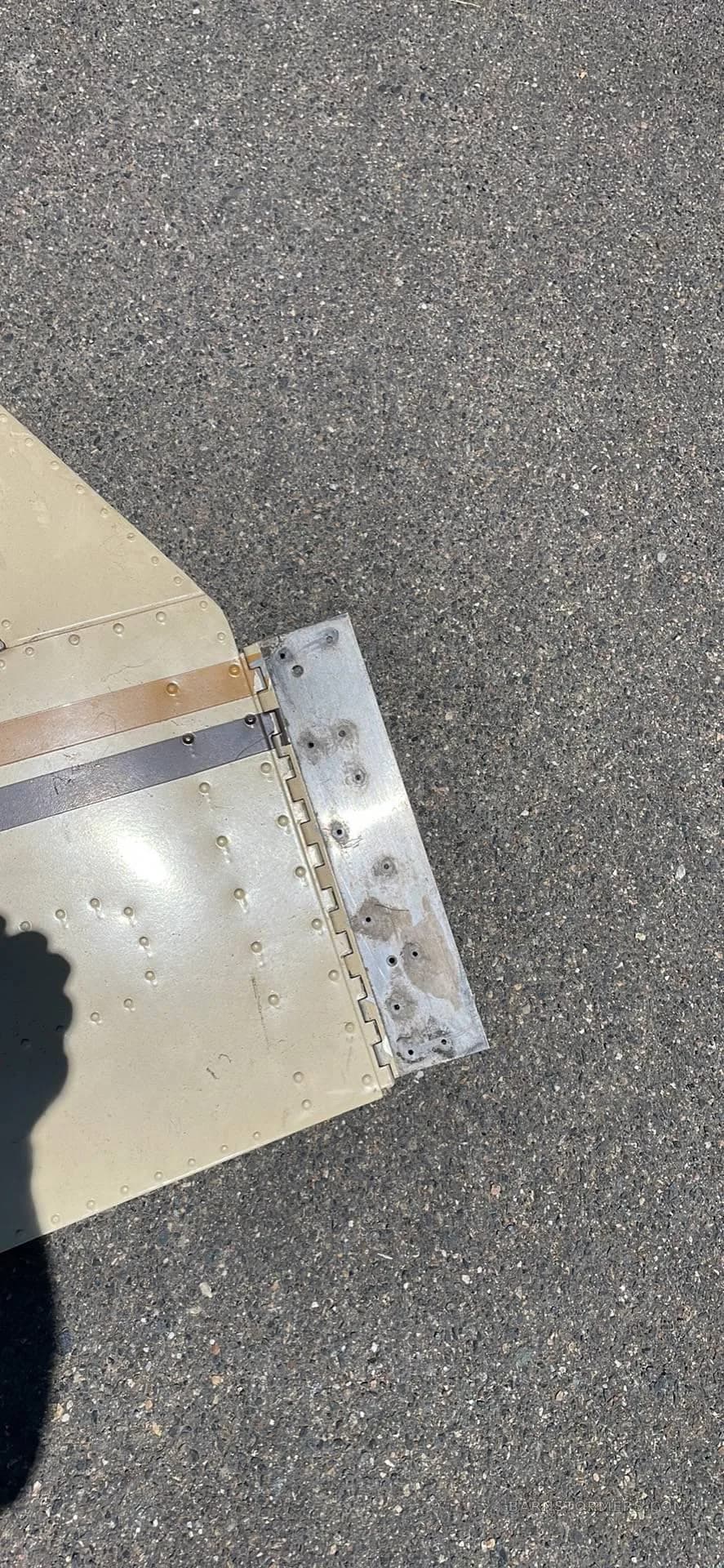 A close-up view of a hinged aircraft component, possibly a flap or aileron, on asphalt.