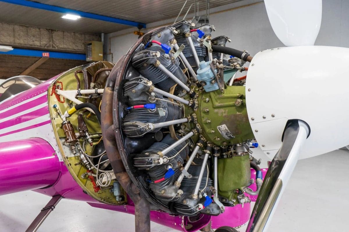 Close-up of the engine and propeller of a pink and white Sukhoi Su-26 aircraft.