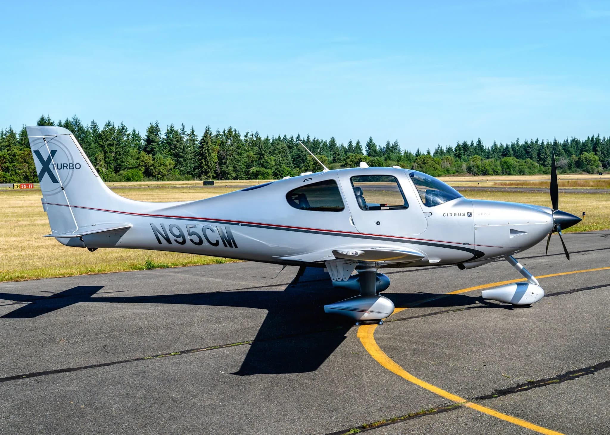 A silver Cirrus SR22T aircraft with registration N95CM parked on an airfield, viewed from the side.