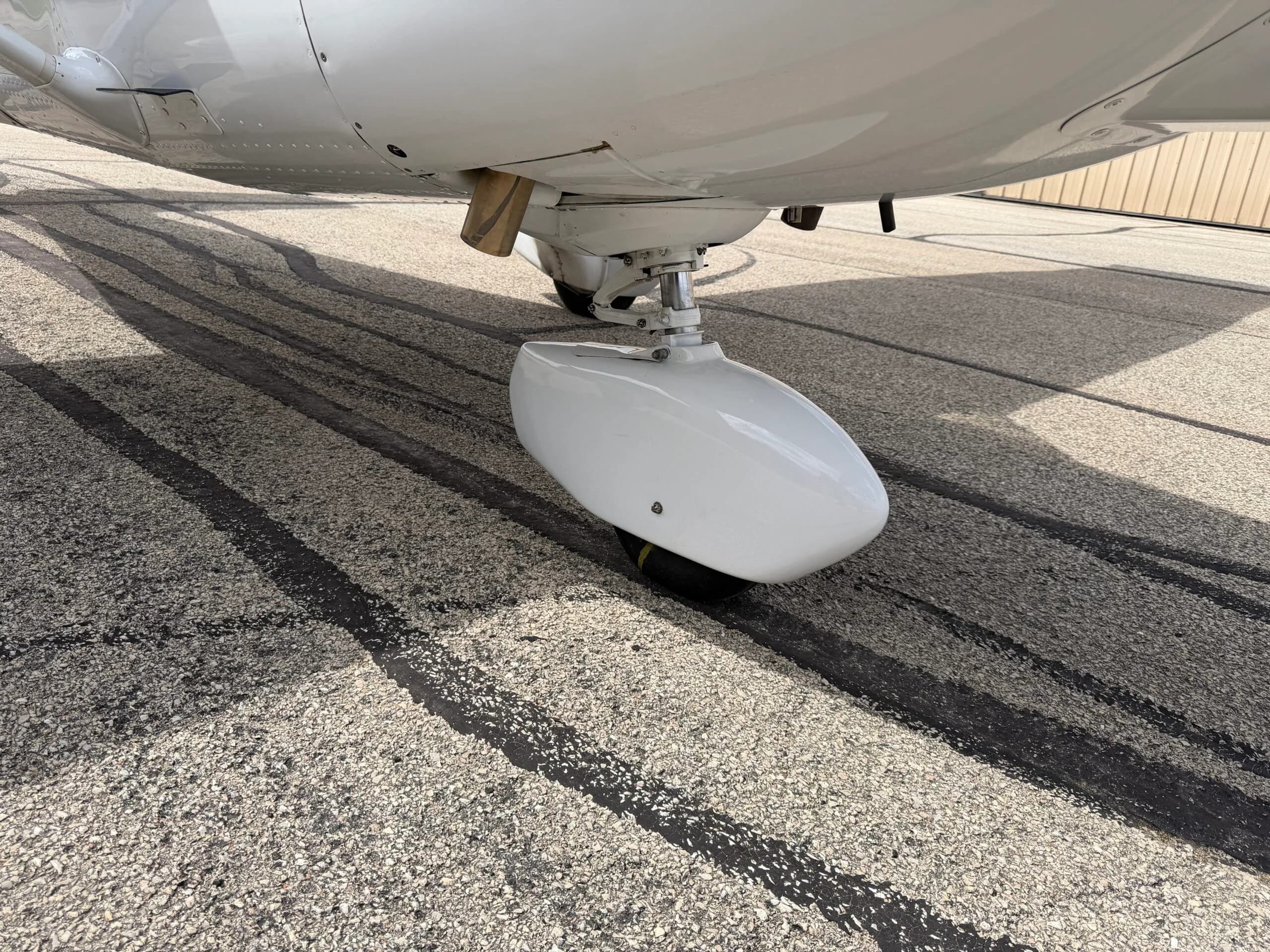 A close-up view of the white nose landing gear fairing of the aircraft.