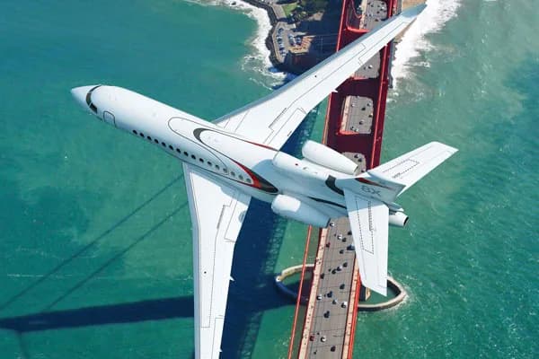 A white Dassault Falcon 8X business jet with red accents flying over the Golden Gate Bridge.