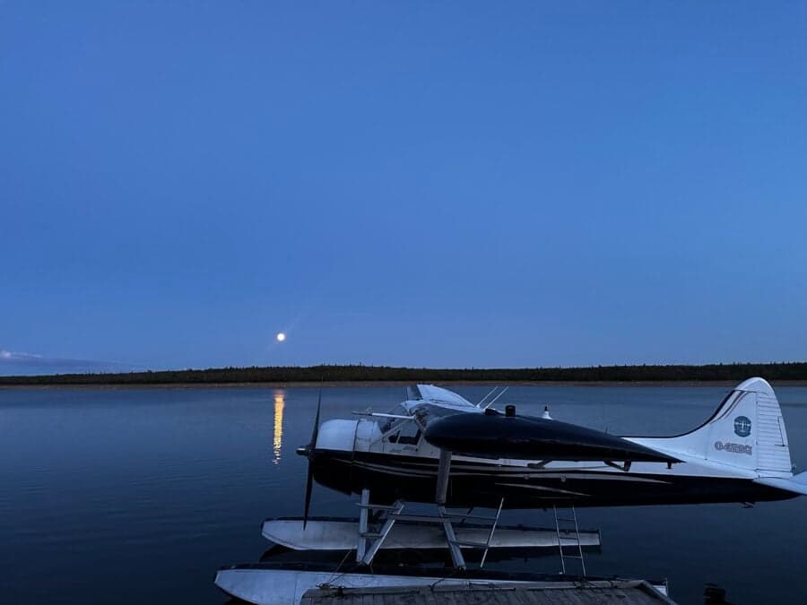 A de Havilland Beaver floatplane is shown on the water at dusk.
