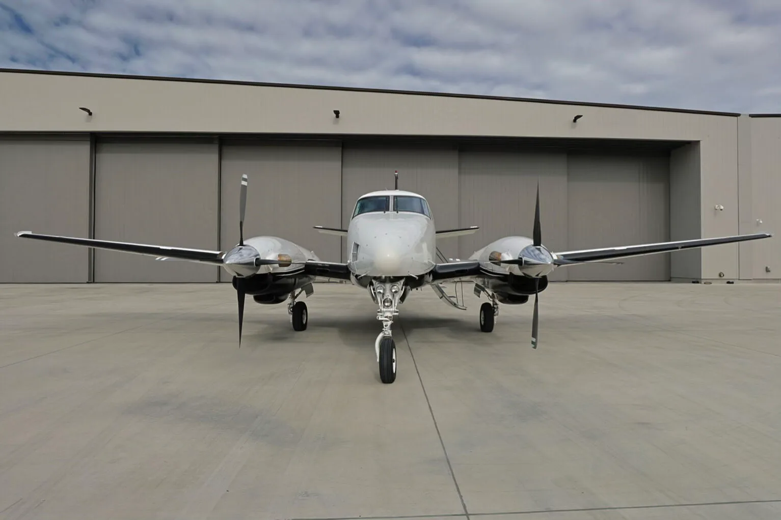 A front view of the N77CE twin-engine turboprop aircraft with a silver and black paint scheme on an airfield.