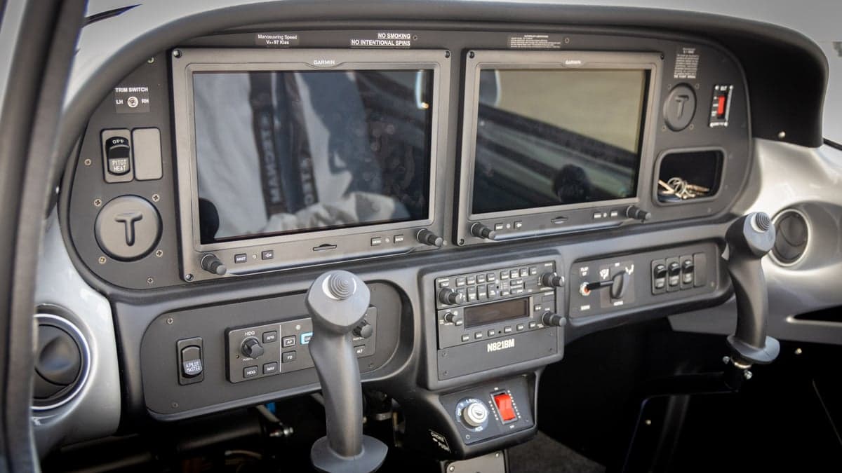 A wide view of the aircraft's cockpit, featuring two large Garmin displays, a radio stack, and control sticks.