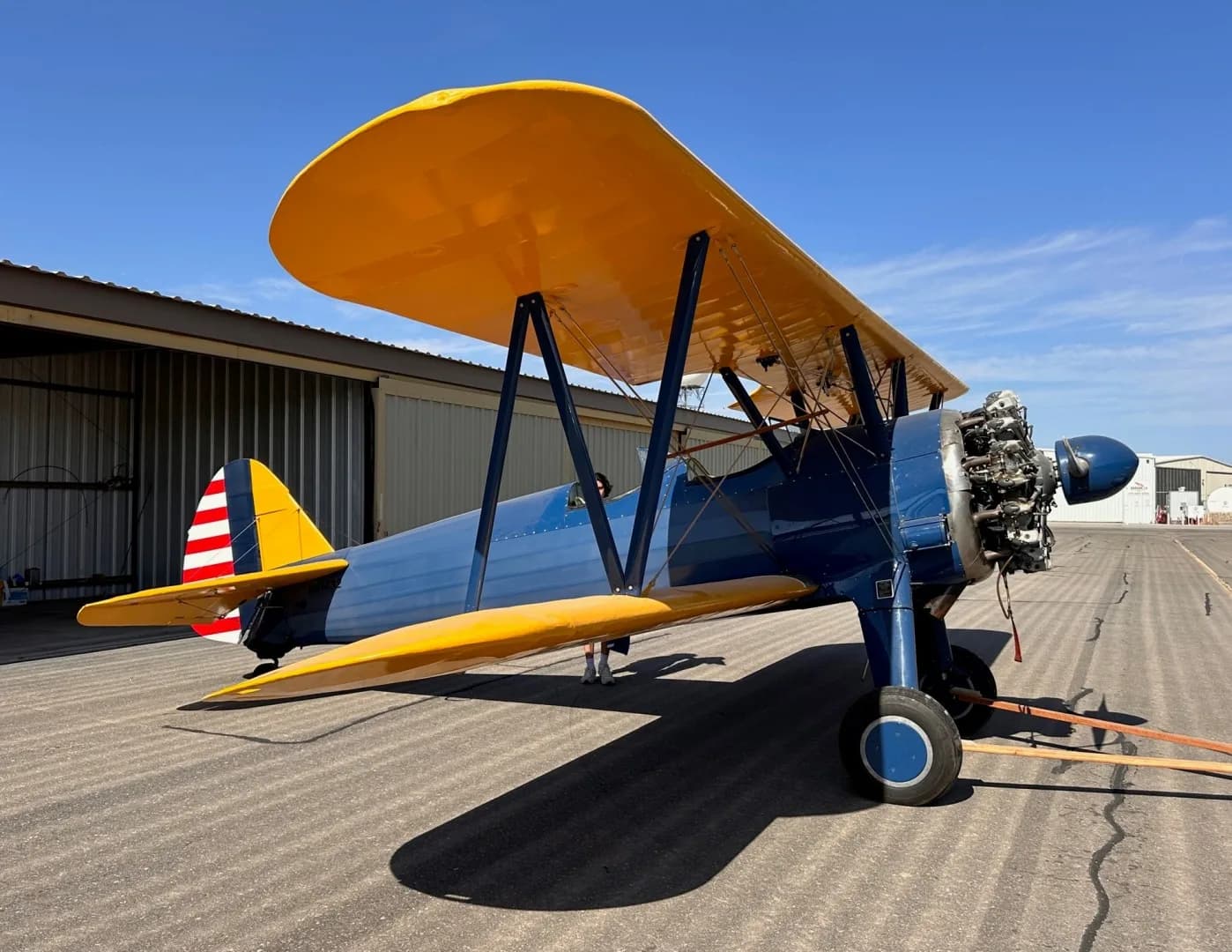 A blue biplane with yellow wings and a radial engine, parked on an airfield tarmac.