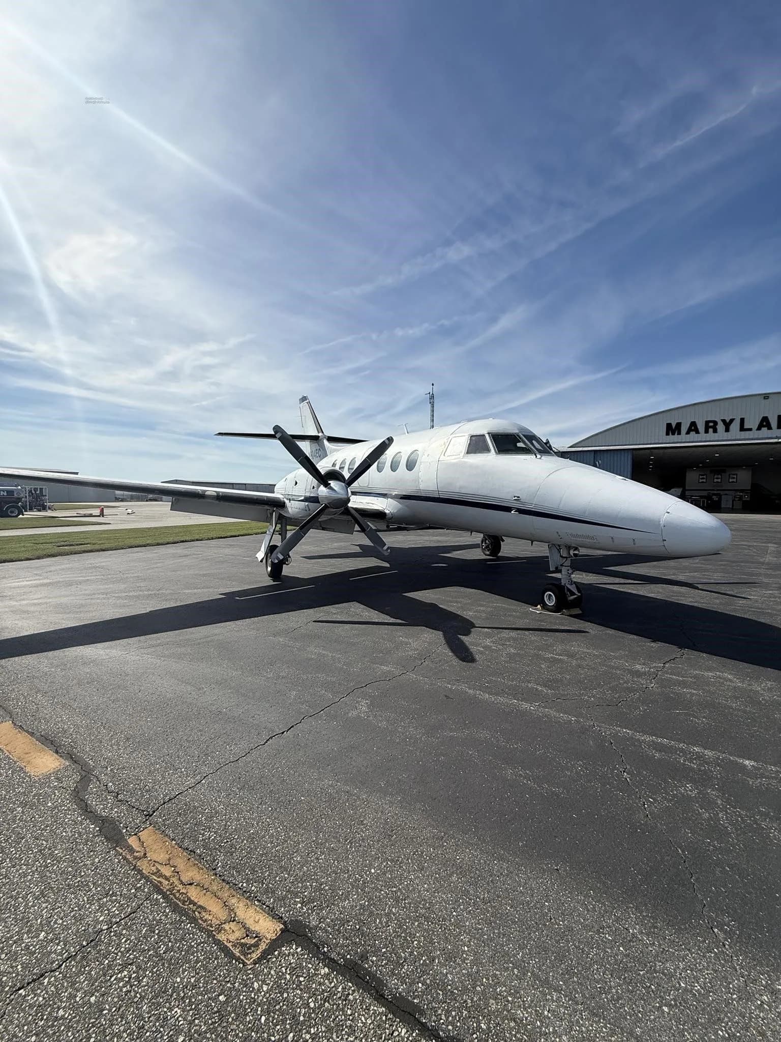 A front-quarter view of a white Jetstream 31 aircraft with blue accents, tail number N604EC, parked on an asphalt tarmac in front of a "MARYLAND AIR" hangar.