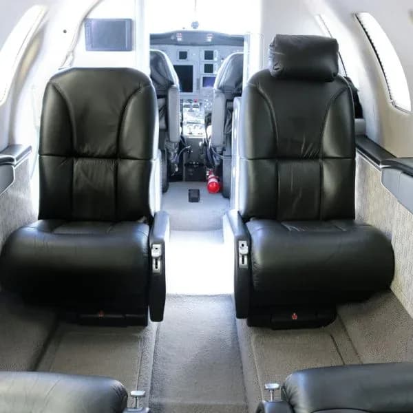 Interior view of a private jet cabin with black leather seats looking forward towards the cockpit.
