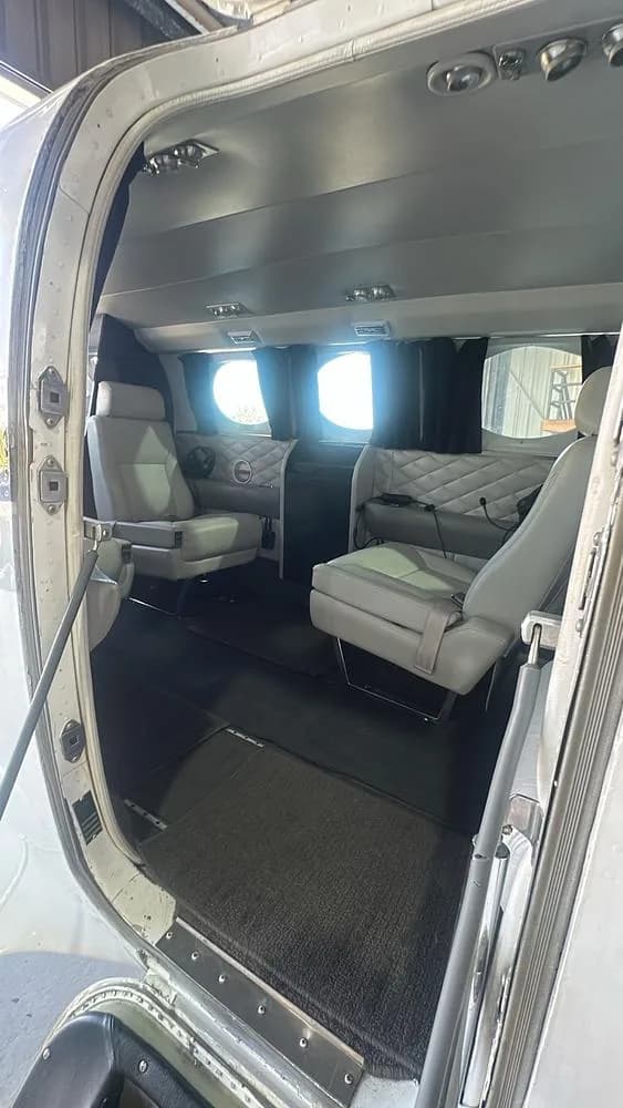 A view into the cabin of a Cessna 421 aircraft from the open entry door, showing light grey seats and quilted side panels.