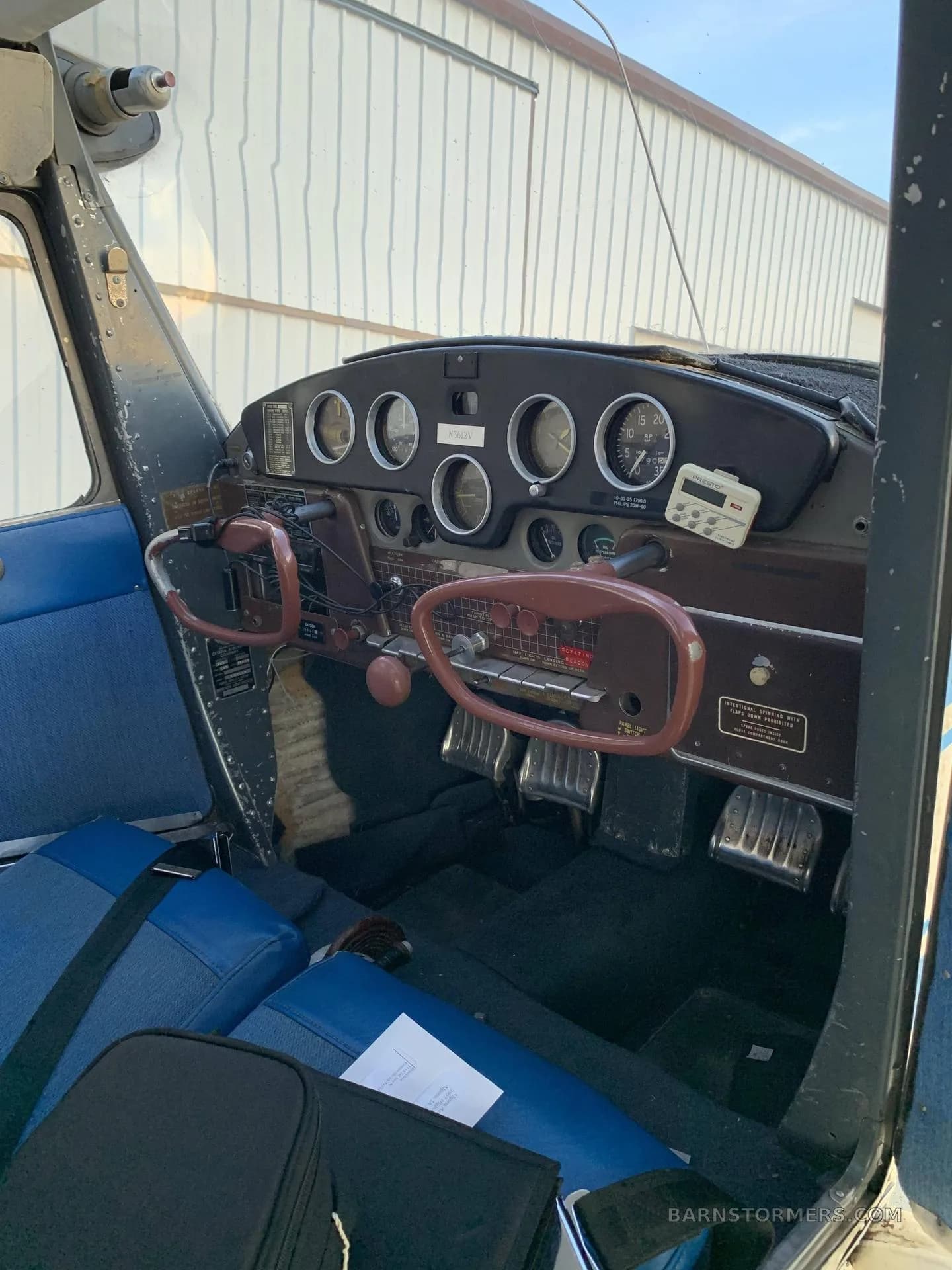 The cockpit of a Cessna 170B, showing the instrument panel, brown yokes, and blue fabric seats.