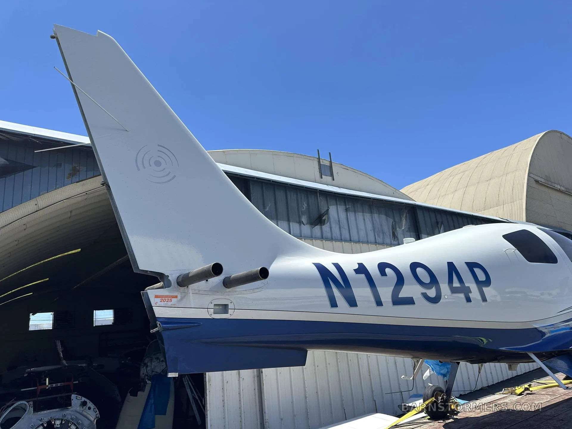 A rear-side view of a white and blue Columbia 400 aircraft, displaying the tail number N1294P and the vertical stabilizer, on a trailer.