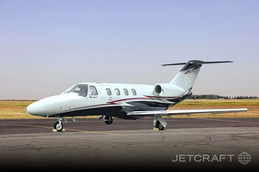 A white business jet with black and red swooping livery on a tarmac under a clear sky.