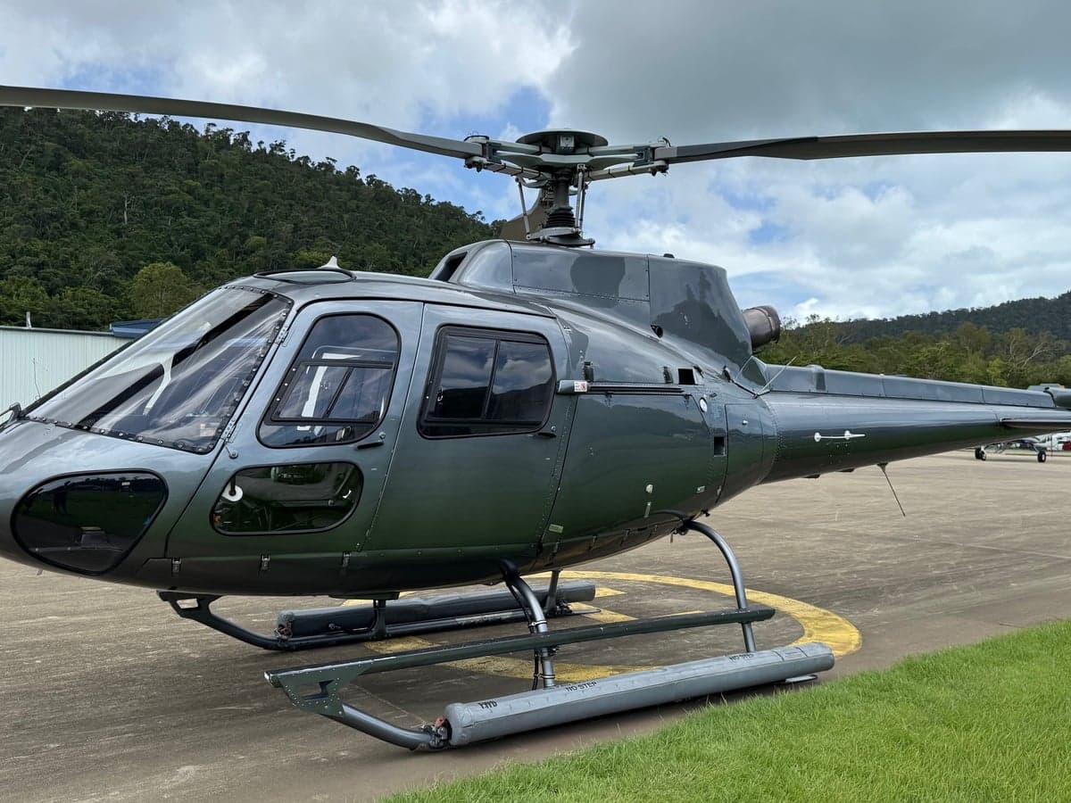 A gray helicopter parked on the tarmac with a green, mountainous background.