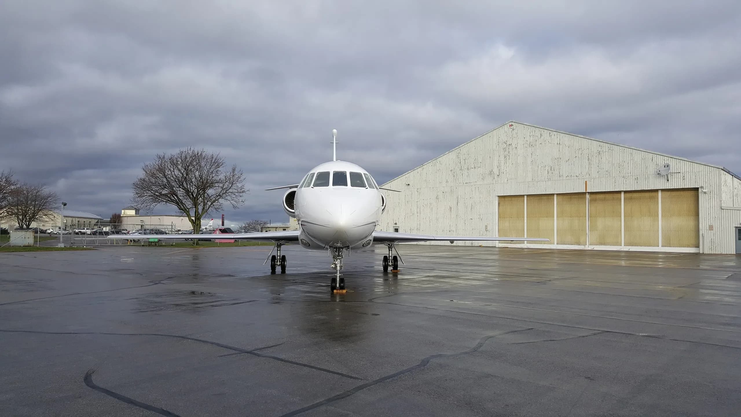 A white Dassault Falcon 2000 business jet, registration N700CH, parked head-on on a wet tarmac in front of a hangar.