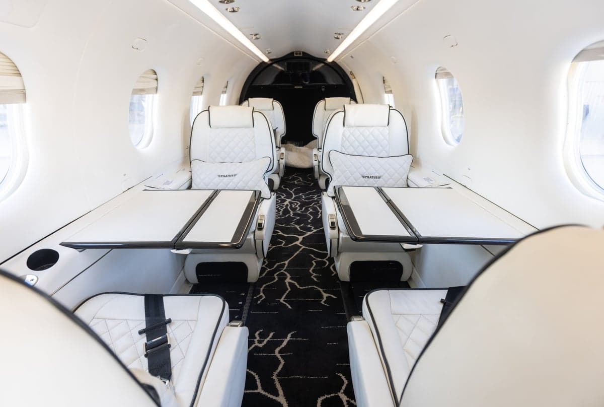 The interior of a Pilatus PC-24 aircraft, featuring white leather seats and tables.