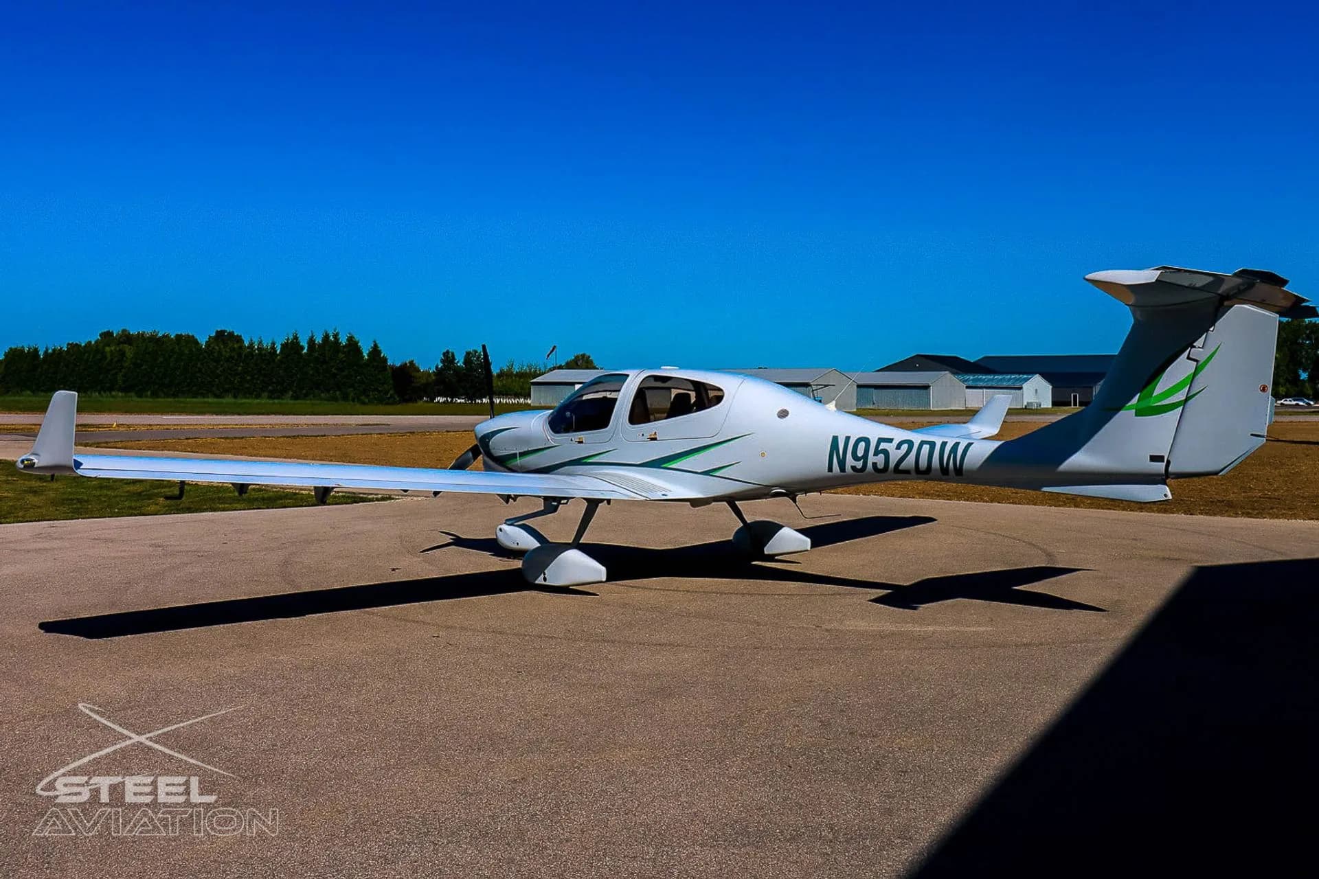 White Diamond DA40 aircraft with green accents and registration N952DW parked on an airfield under a clear blue sky.