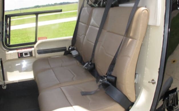 A view of the tan leather rear bench seat with seatbelts in the helicopter's cabin.