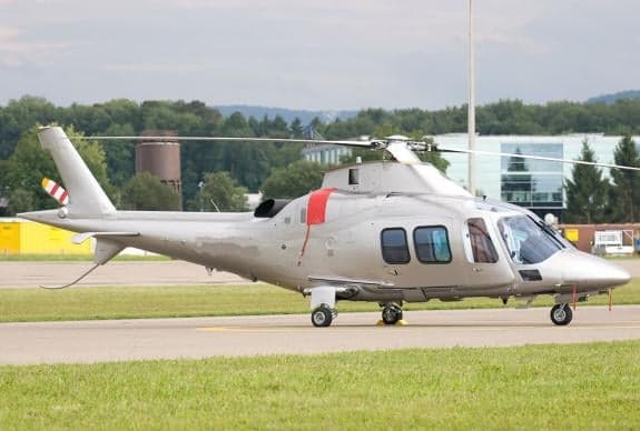 A silver helicopter sits on the tarmac at an airport.