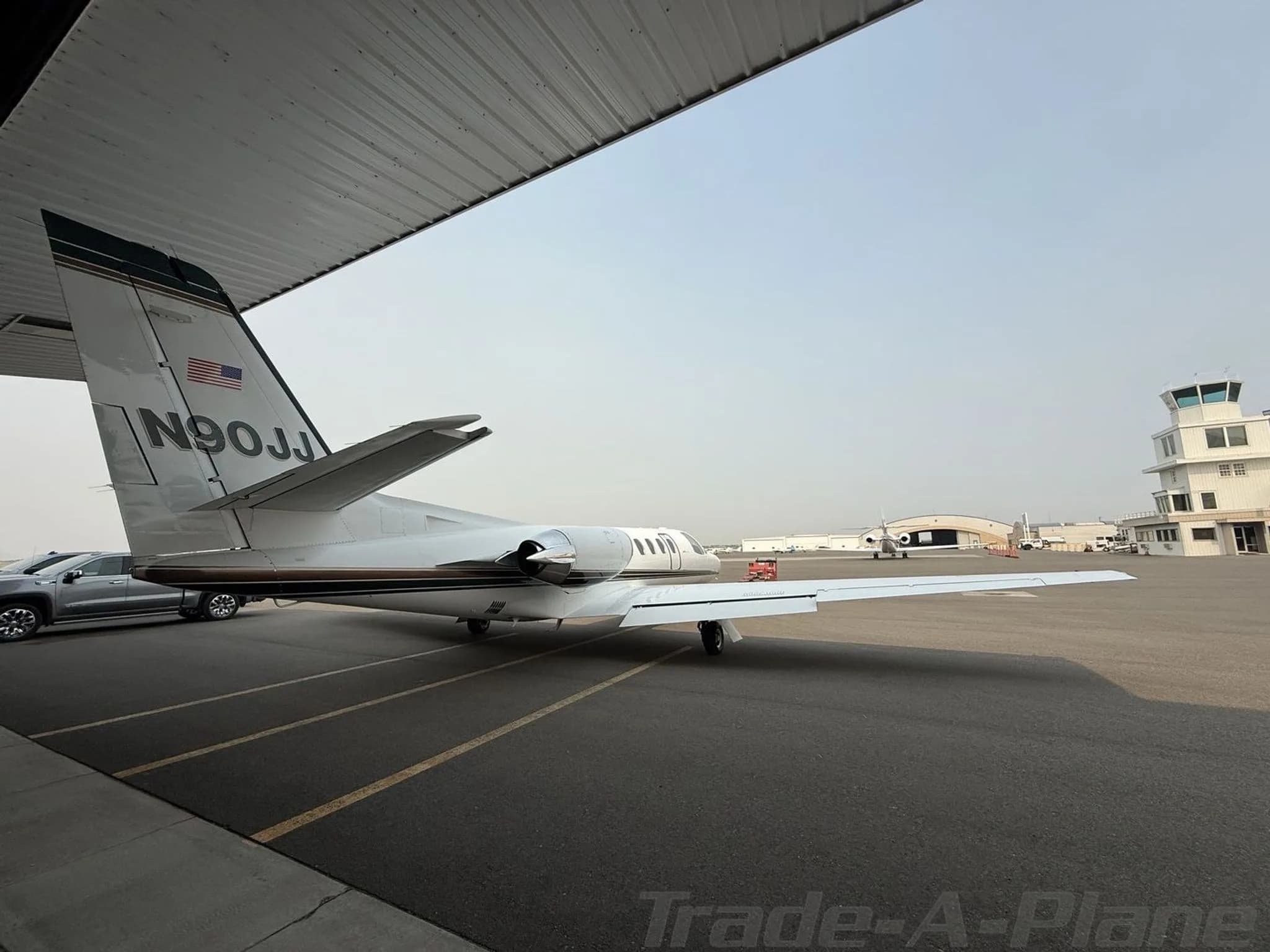 The tail of a white Cessna Citation jet, N90JJ, with a control tower in the background at an airport.