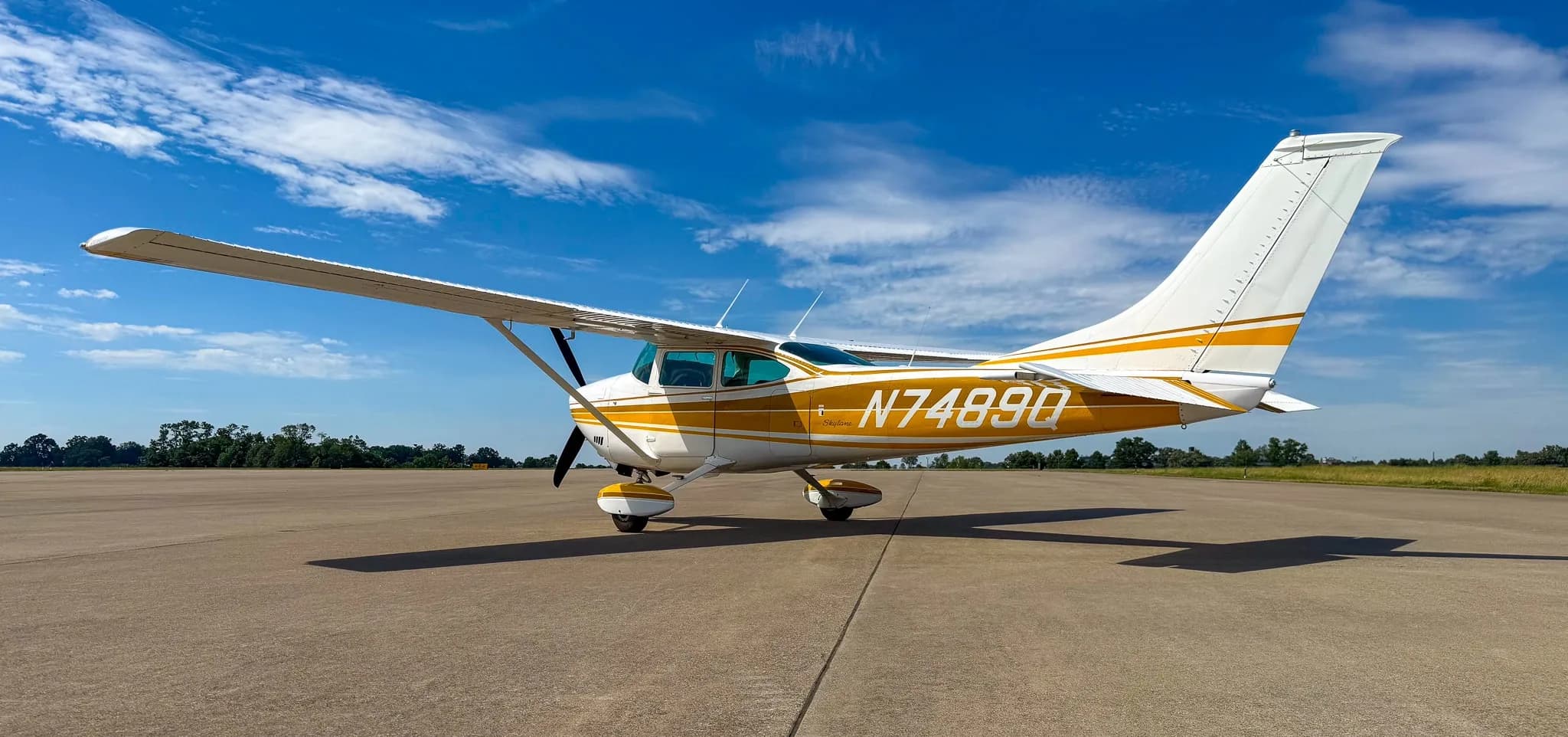 A white and gold Cessna Skylane N7489Q is parked on an airfield tarmac, viewed from the right-rear side.