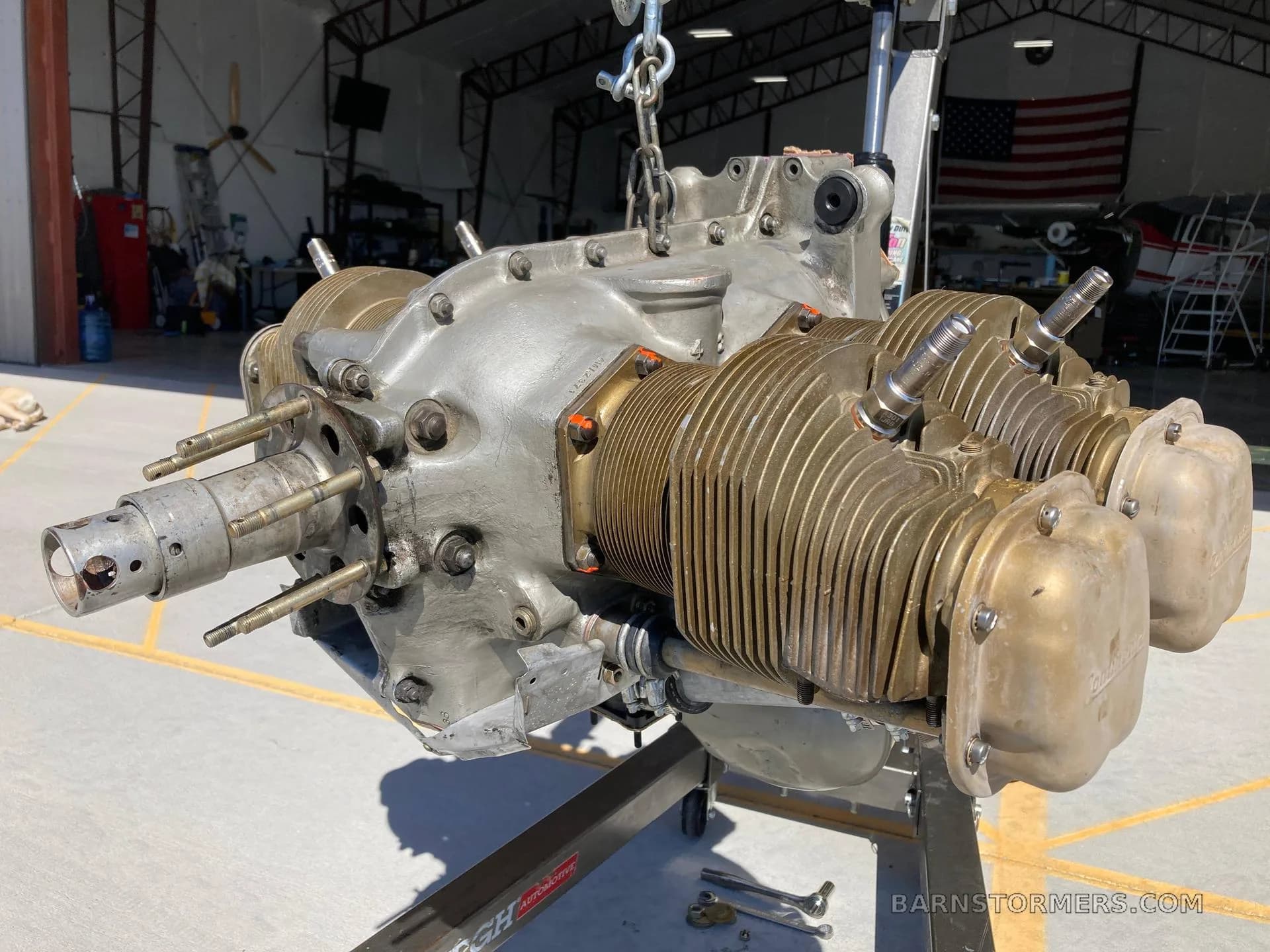 A grey aircraft engine with bronze cylinders on a stand inside a hangar.