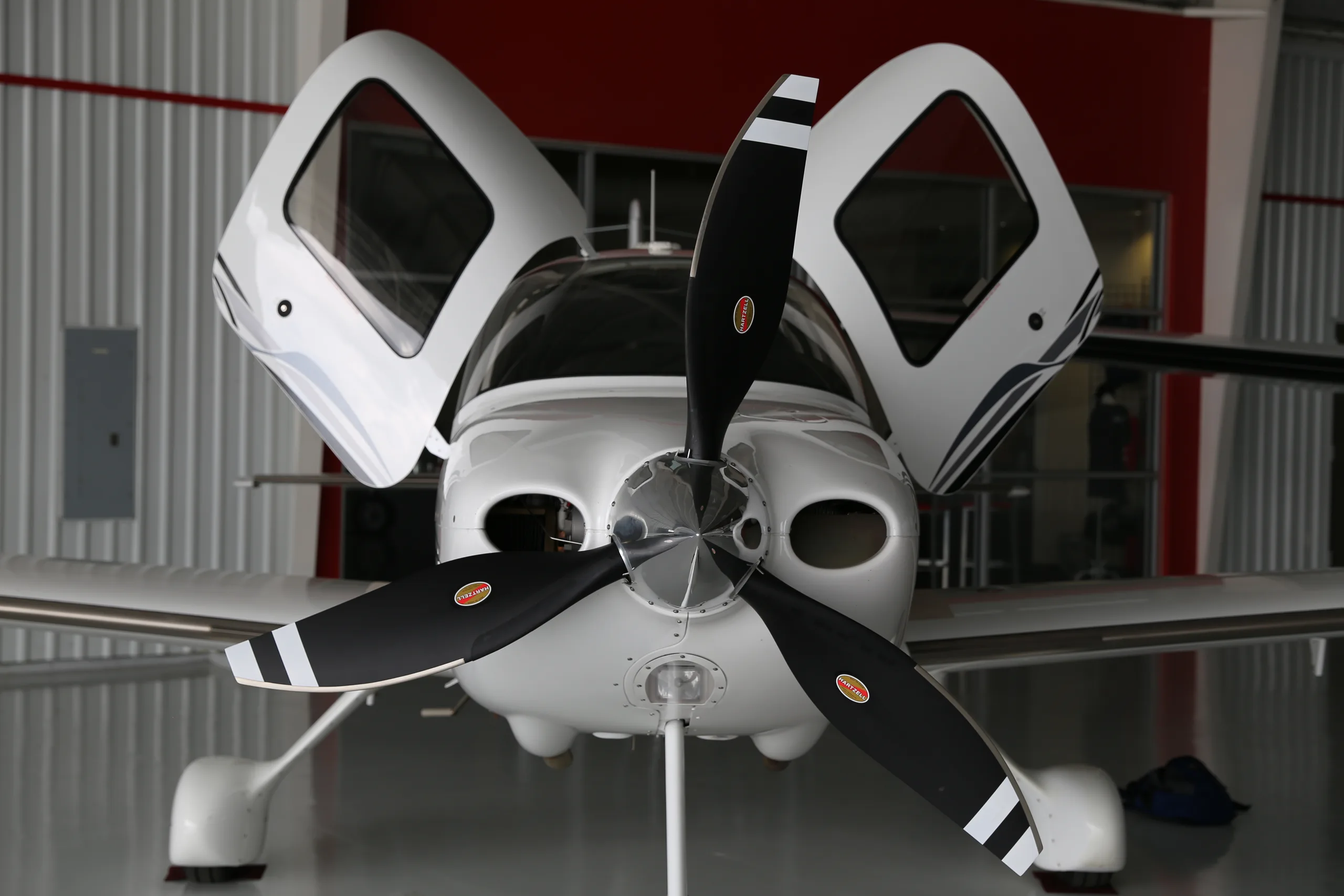 A front view of the white Cirrus SR22T aircraft with its two gull-wing doors open, parked in a hangar.