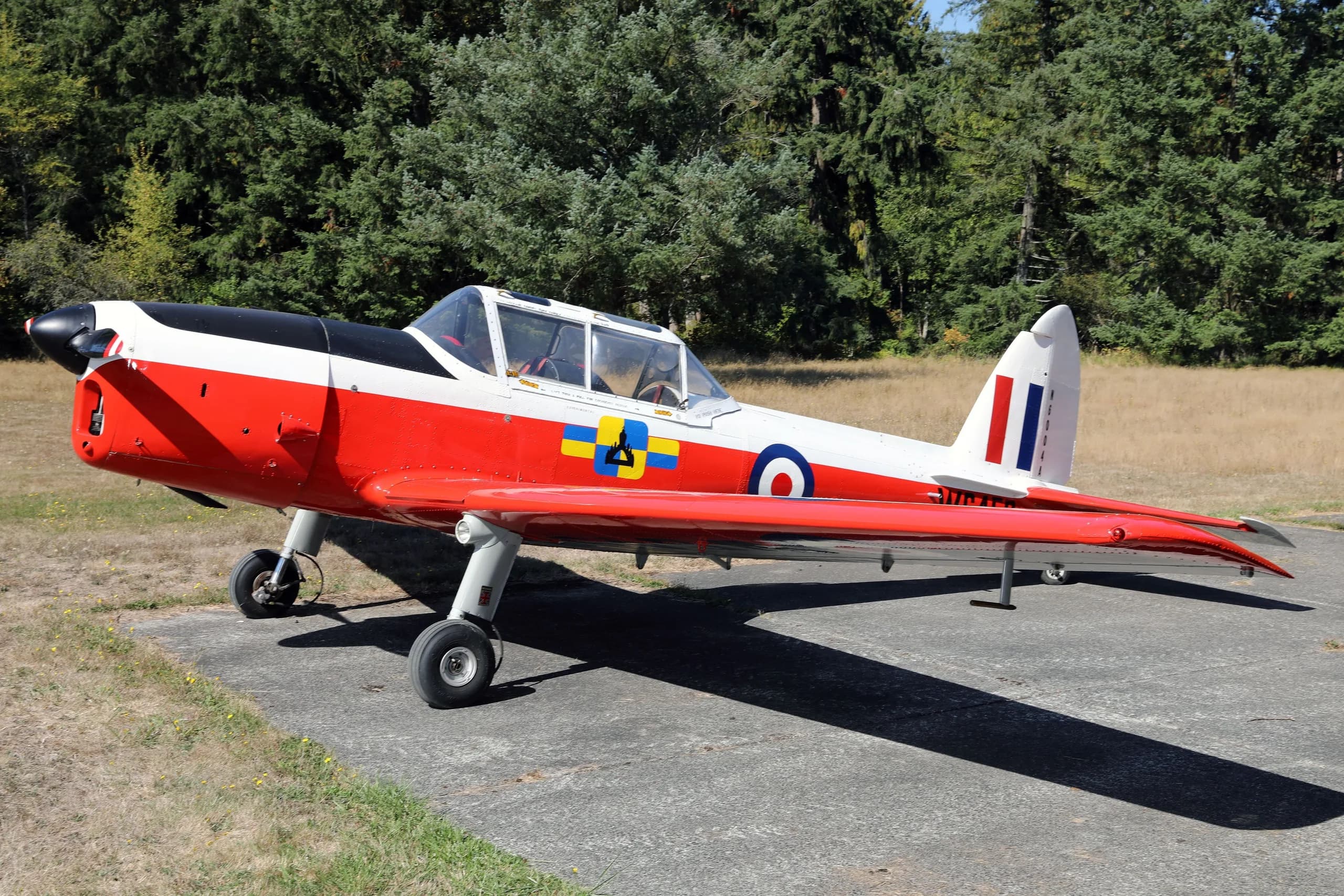 A red, white, and black de Havilland Canada DHC-1 Chipmunk aircraft with British roundels and "WC459" markings, parked on an airfield.