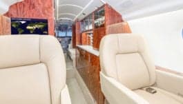 View of the interior cabin with cream-colored leather seats and wood trim.