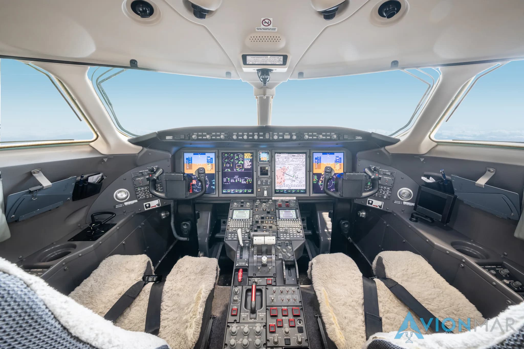 The modern cockpit of a private jet with multiple digital displays, control yokes, and sheepskin seat covers.