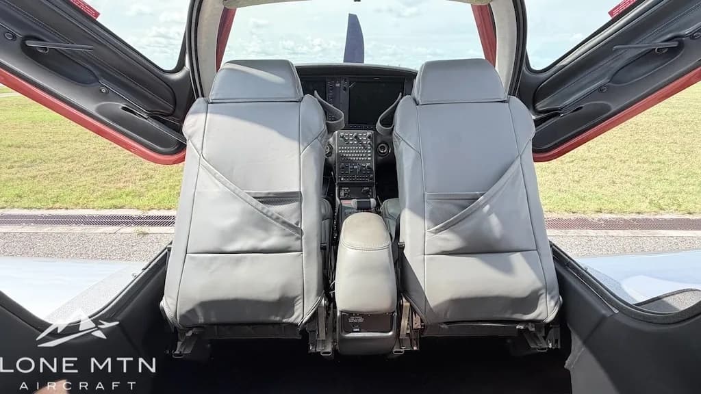 The gray leather front seats of a Cirrus SR22T aircraft, viewed from the rear, with the cockpit visible between them.