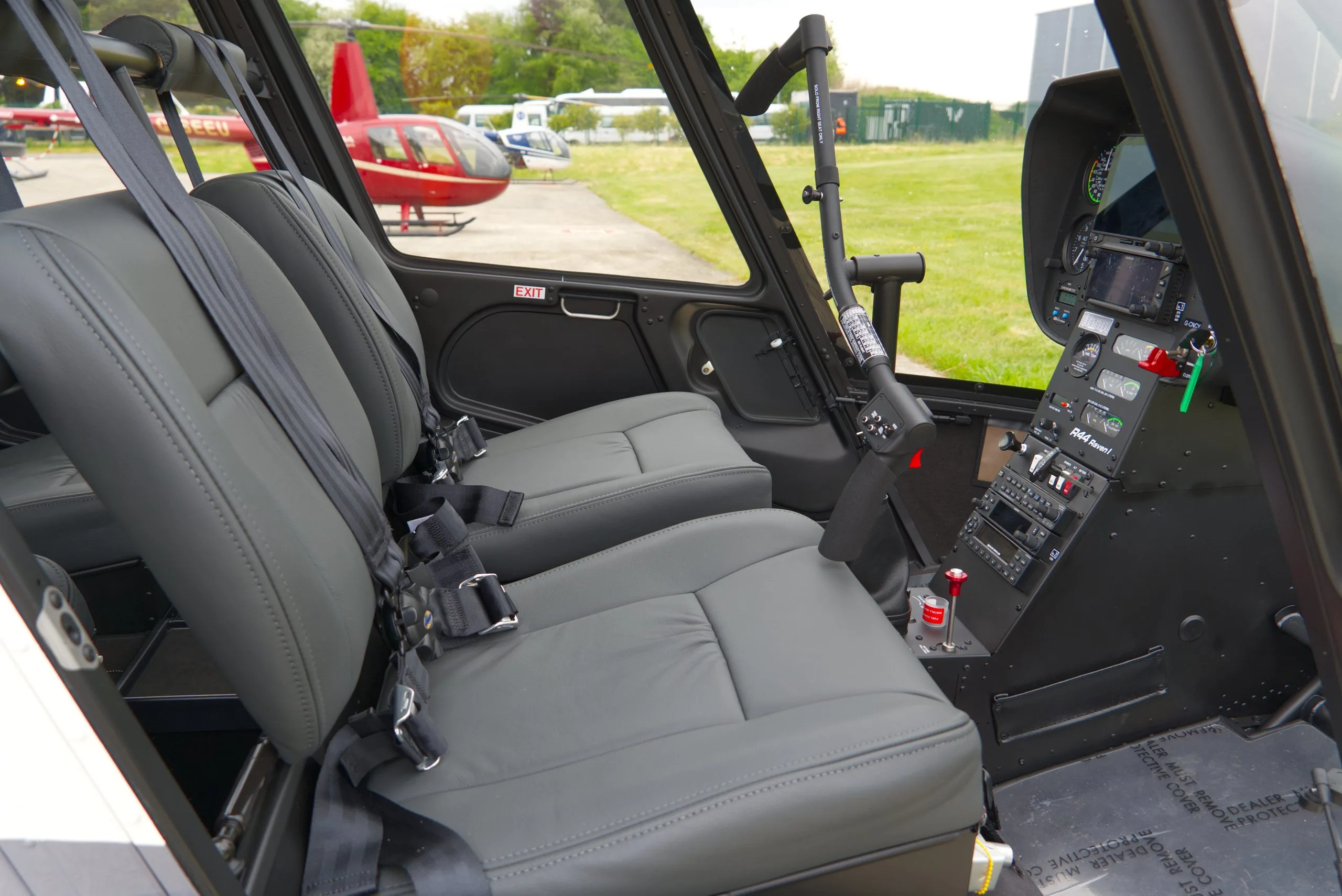 The grey leather interior seats of a helicopter, with a view of the tarmac and other helicopters outside.
