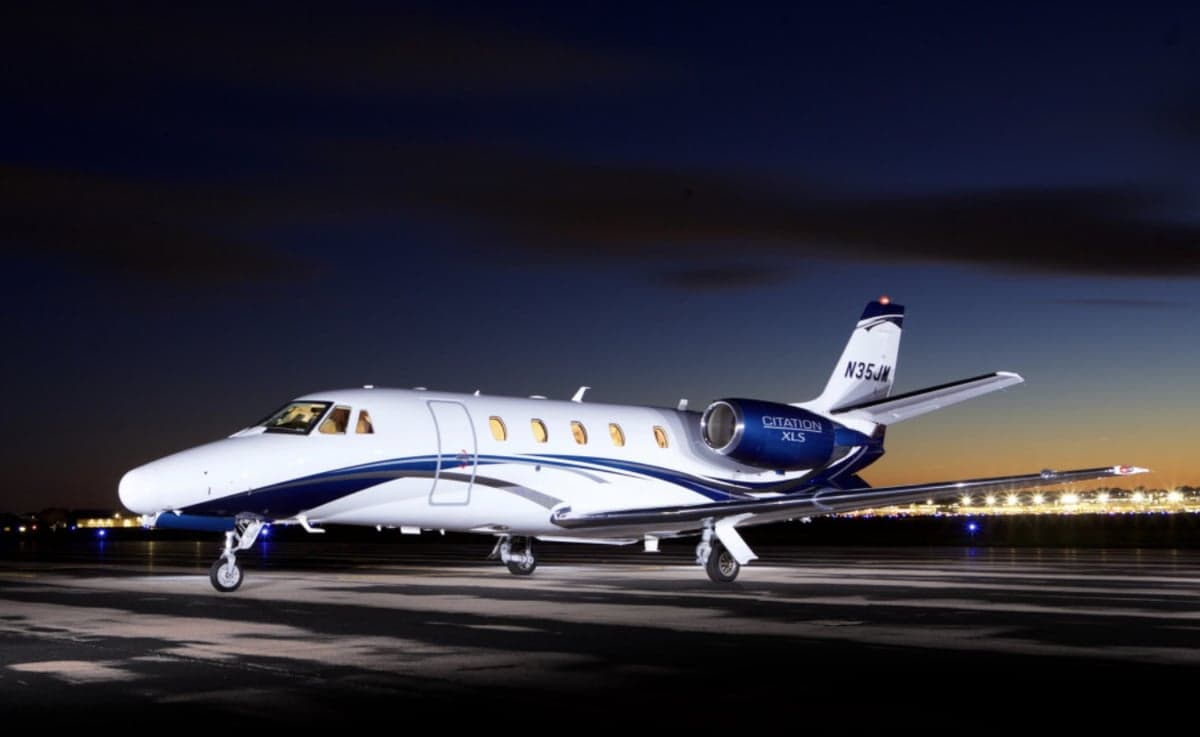 A white and blue Cessna Citation XLS on the ramp at dusk.