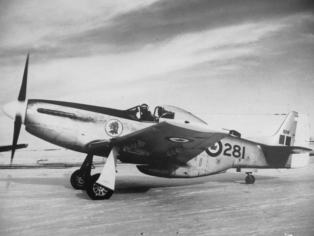 A vintage P-51 Mustang with Canadian markings on a snowy airfield.