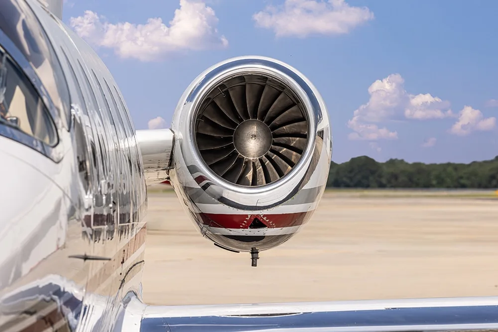 Close-up of a private jet's polished engine nacelle and fan blades on an airfield.