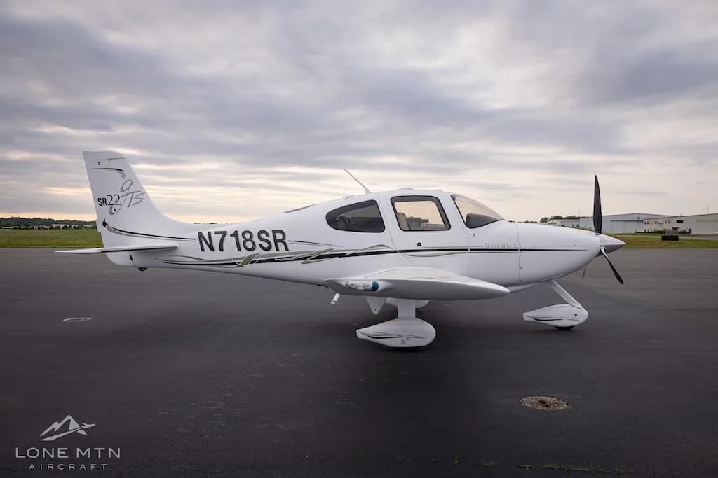Side view of a white Cirrus SR22T aircraft with black and gold accents parked on an asphalt tarmac.