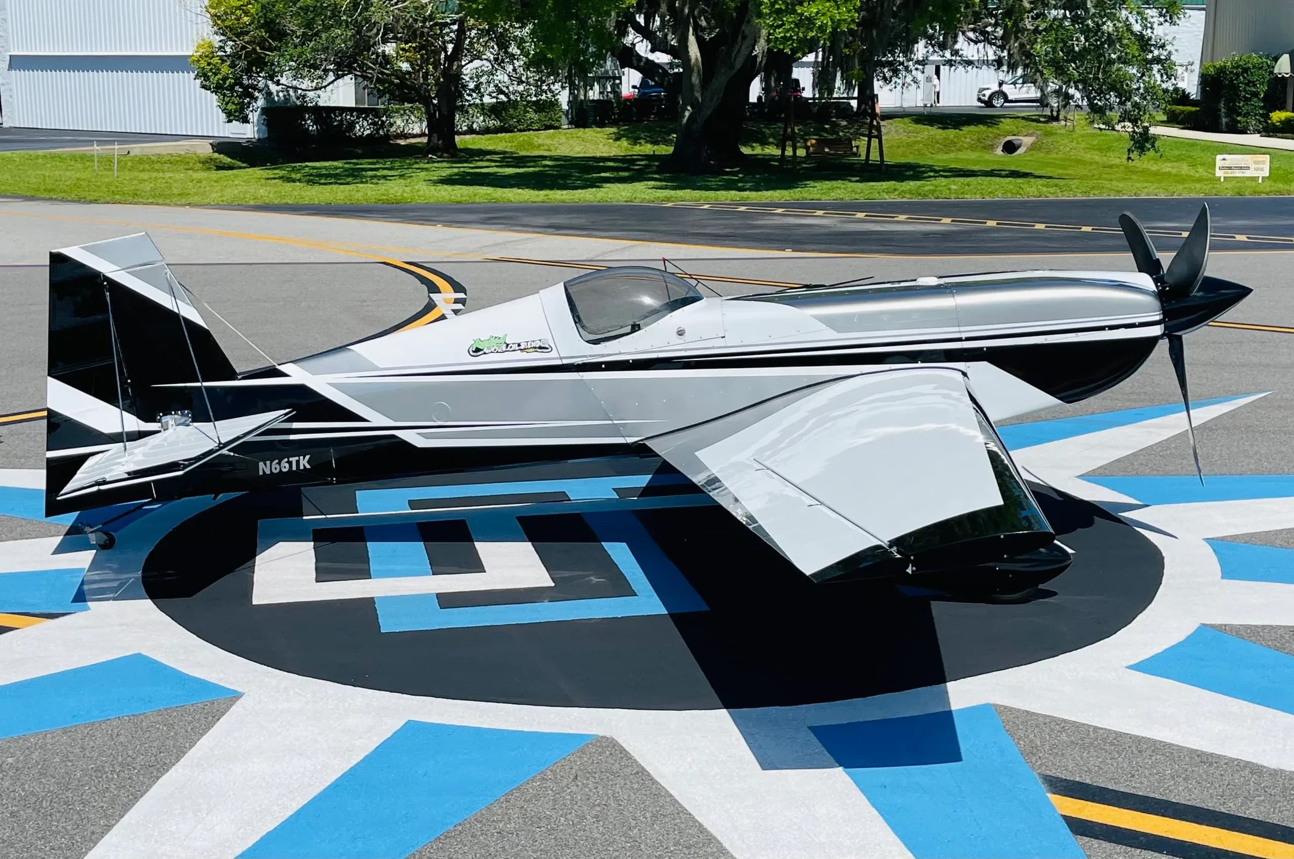 A side view of a black, white, and grey aerobatic aircraft (N66TK) parked on a patterned airfield.