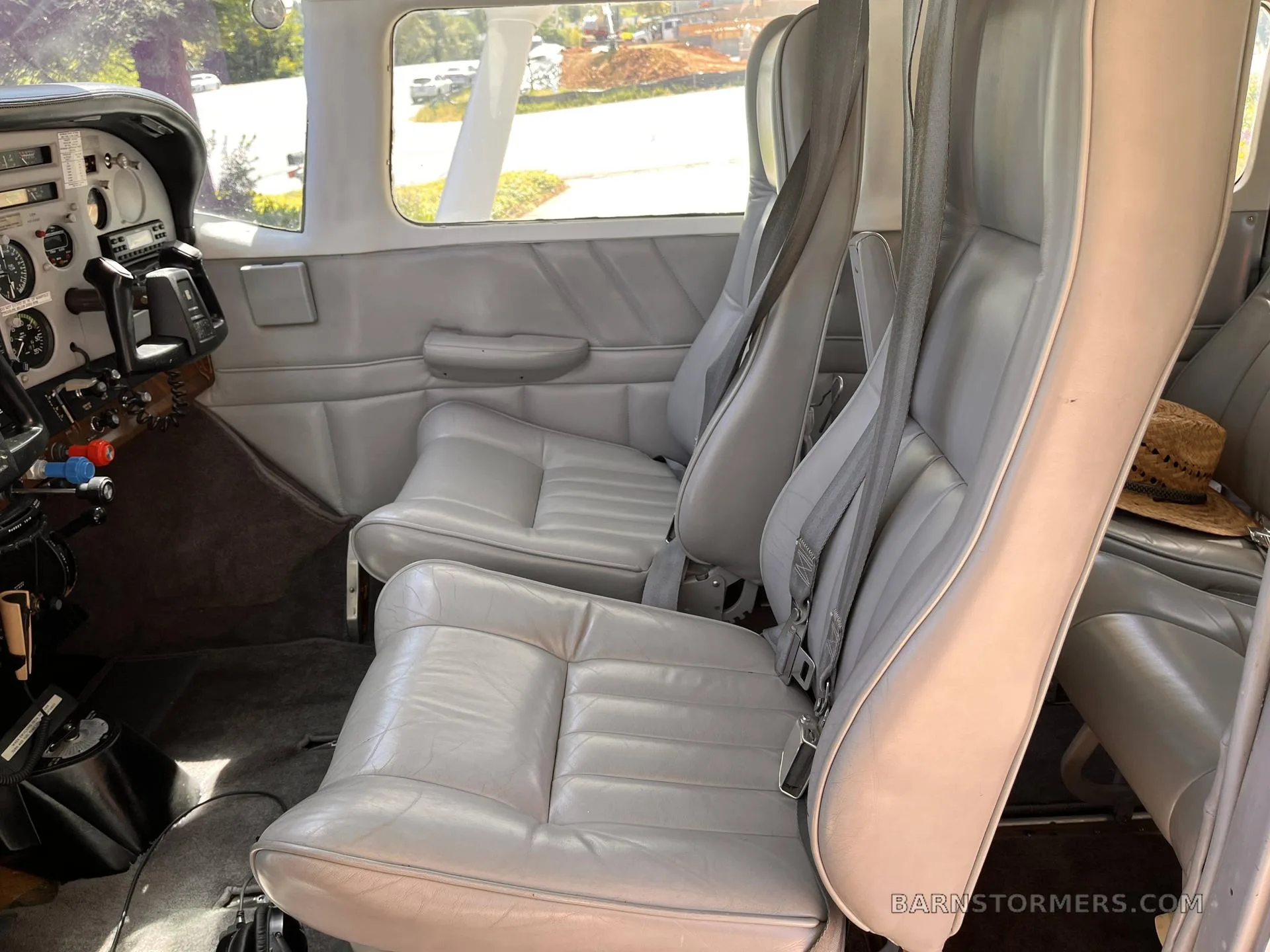 The light gray leather front and middle row seats of an aircraft cabin, with a straw hat on the right rear seat.