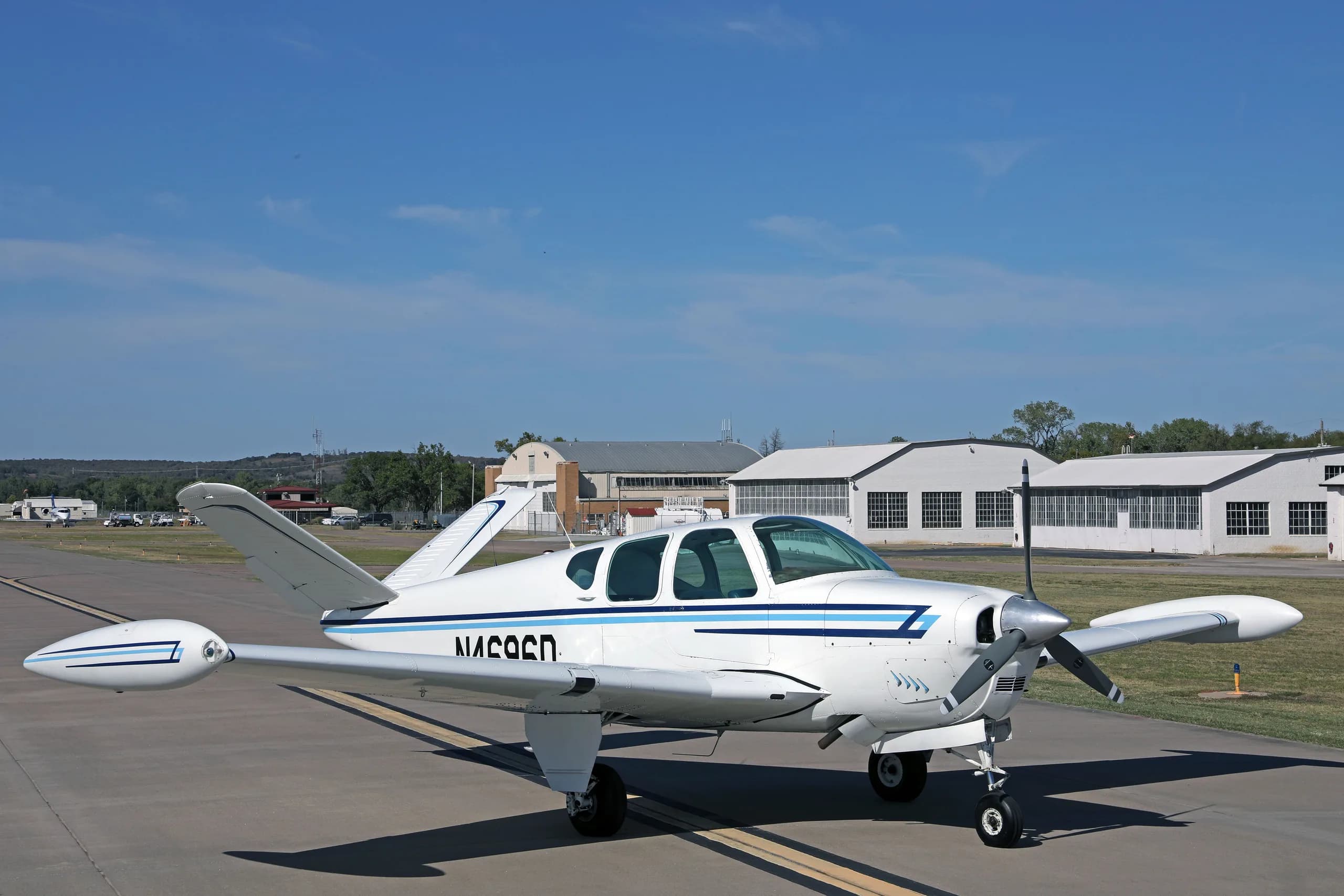 A front-side view of a white single-engine aircraft with blue stripes, registration N4696D, on an airfield.