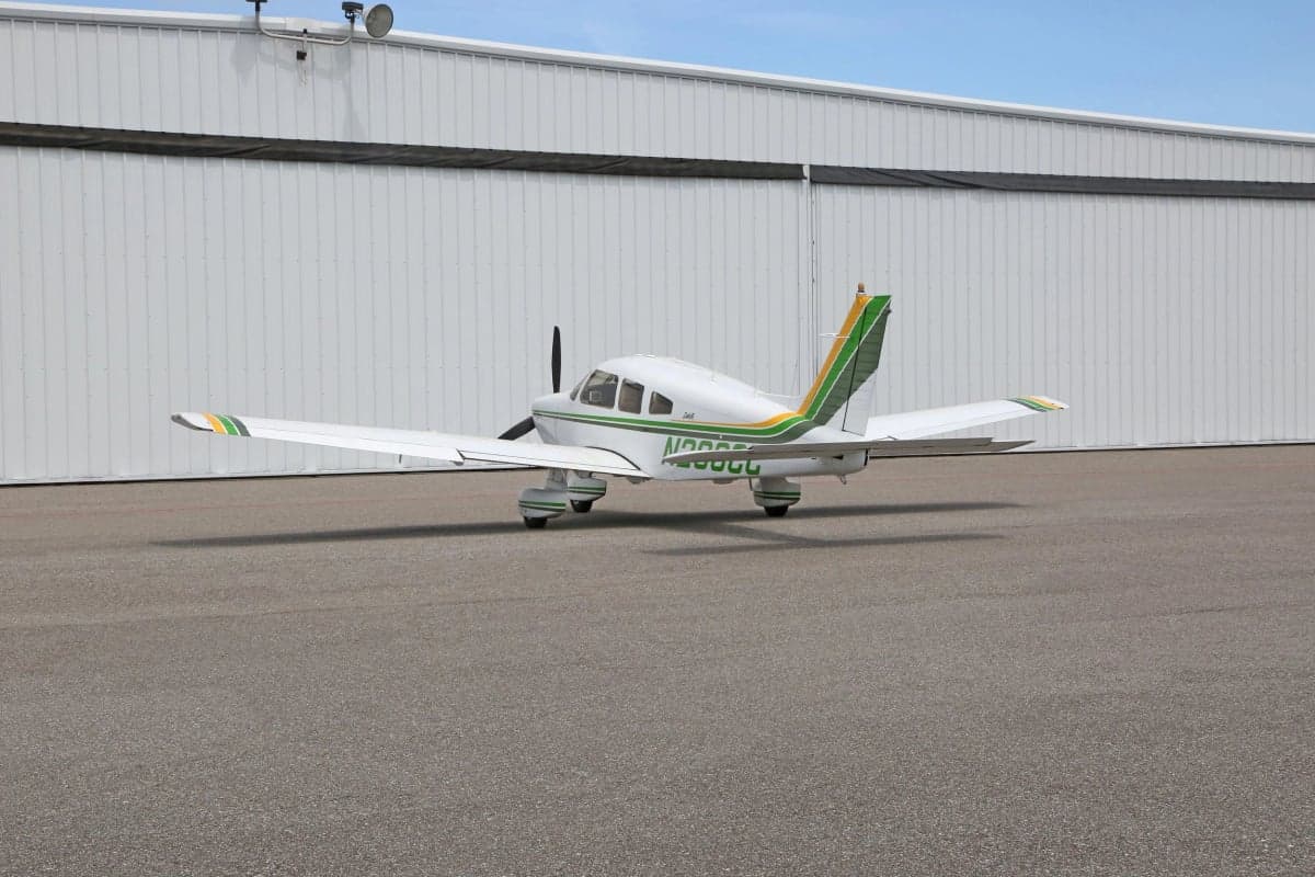 Side rear view of a white and green Piper Dakota aircraft on the tarmac.