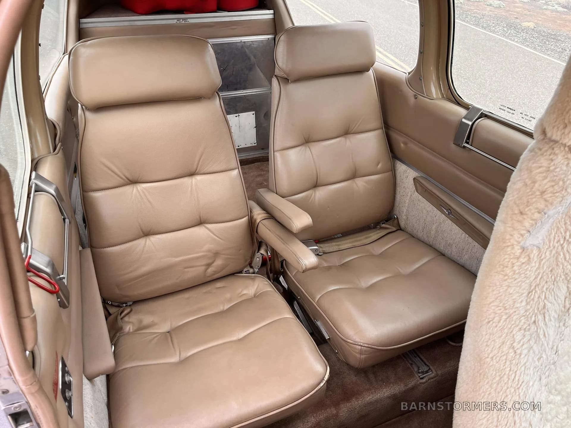 The rear cabin of a Beechcraft Bonanza, featuring two tan leather seats with armrests.