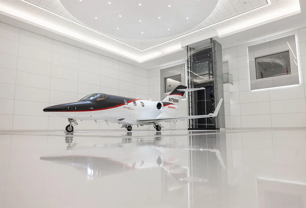 A black and white HondaJet Elite II (N798NH) with red accents is shown from a low angle in a modern white showroom with a reflective floor.