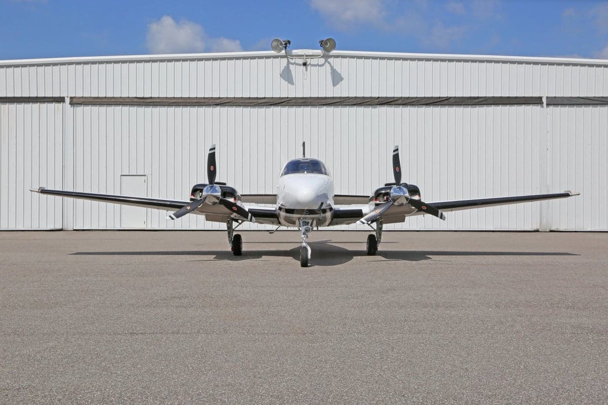 Front view of a Beechcraft Baron G58 aircraft on the ground in front of a hangar.