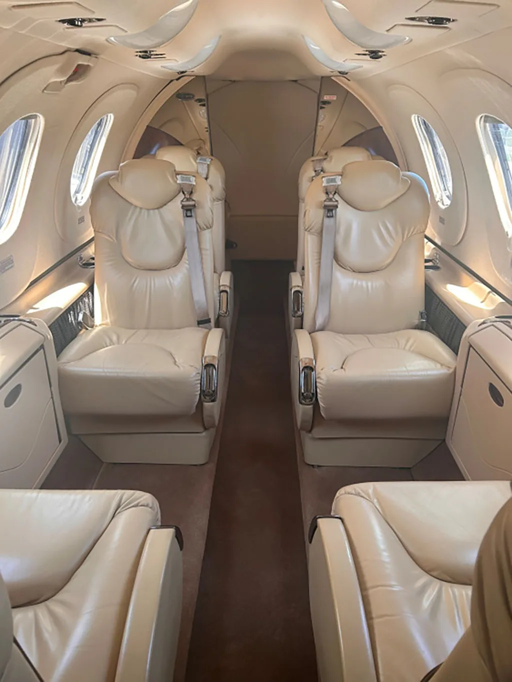 The interior cabin of a private jet with light tan leather seats arranged in a club configuration.