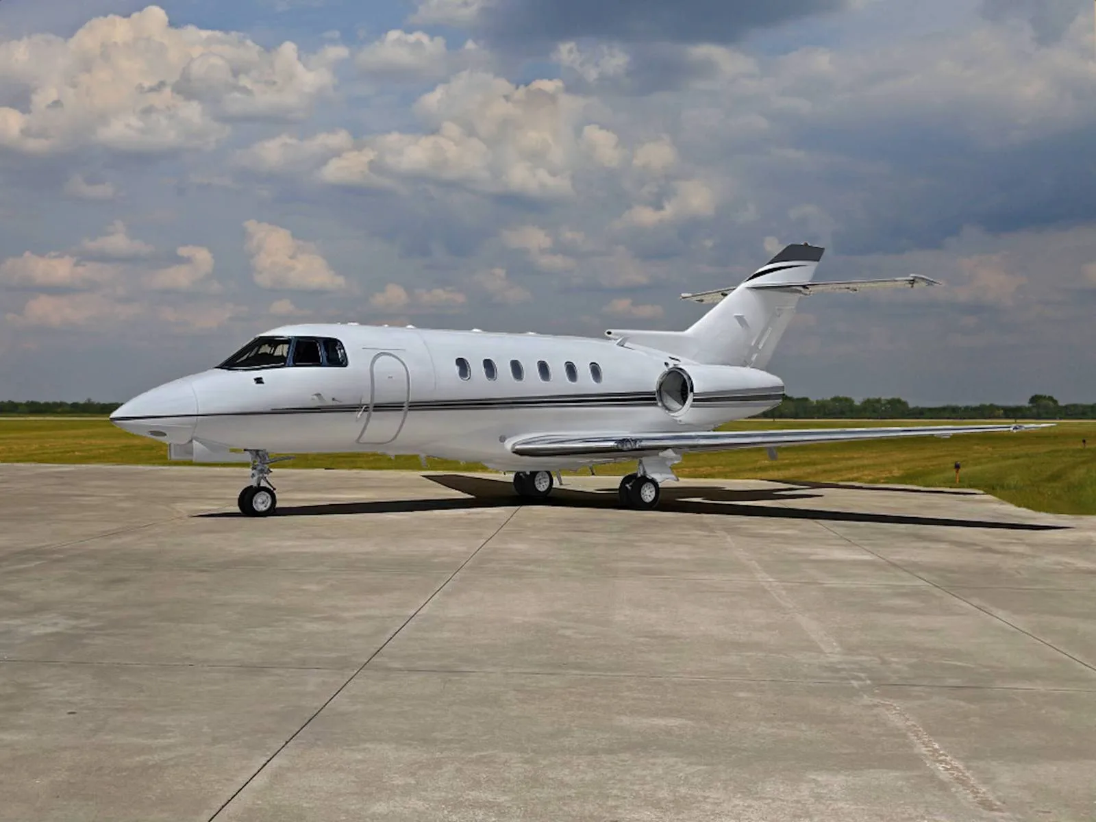 A white jet aircraft is parked on the tarmac under a cloudy sky.