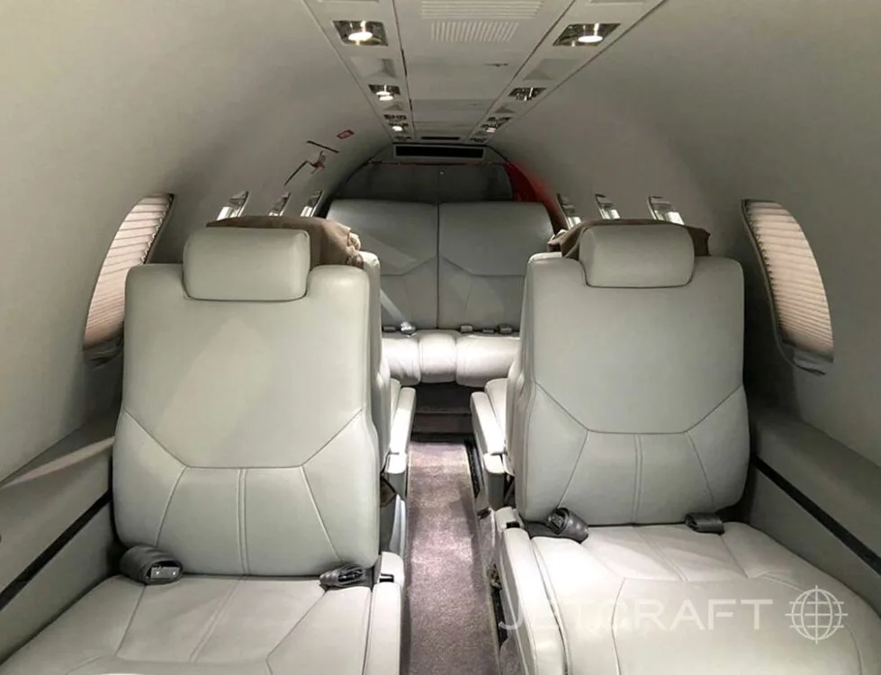 The interior cabin of a business jet, featuring light gray leather seats arranged in a club configuration.