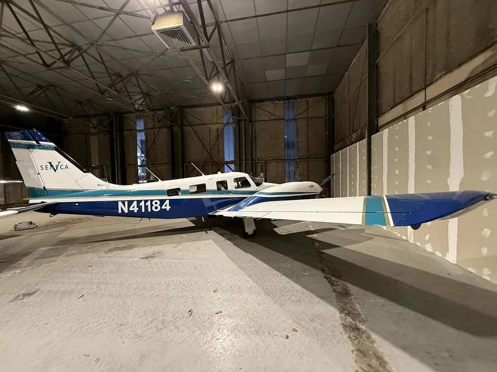Left side view of a Piper Seneca aircraft N41184, with white and blue livery, inside a hangar.