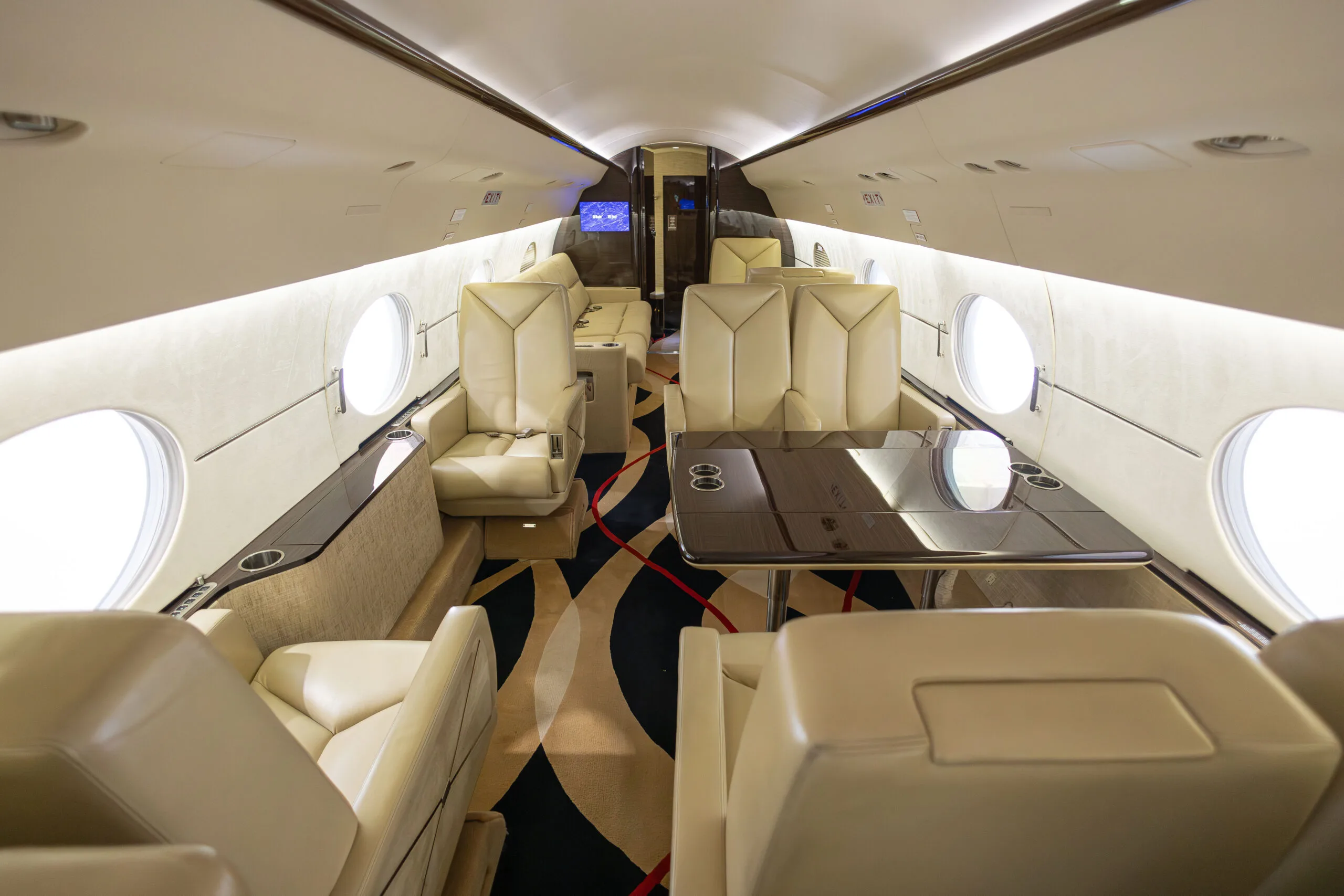 Aircraft interior featuring leather seats, a table, and patterned carpet.