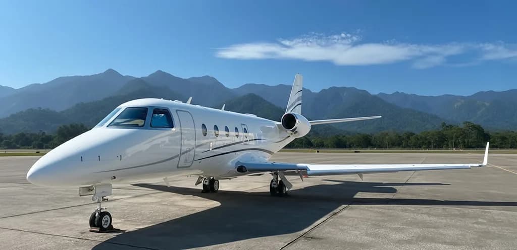 A white business jet with black and grey stripes is parked on an tarmac under a clear blue sky.