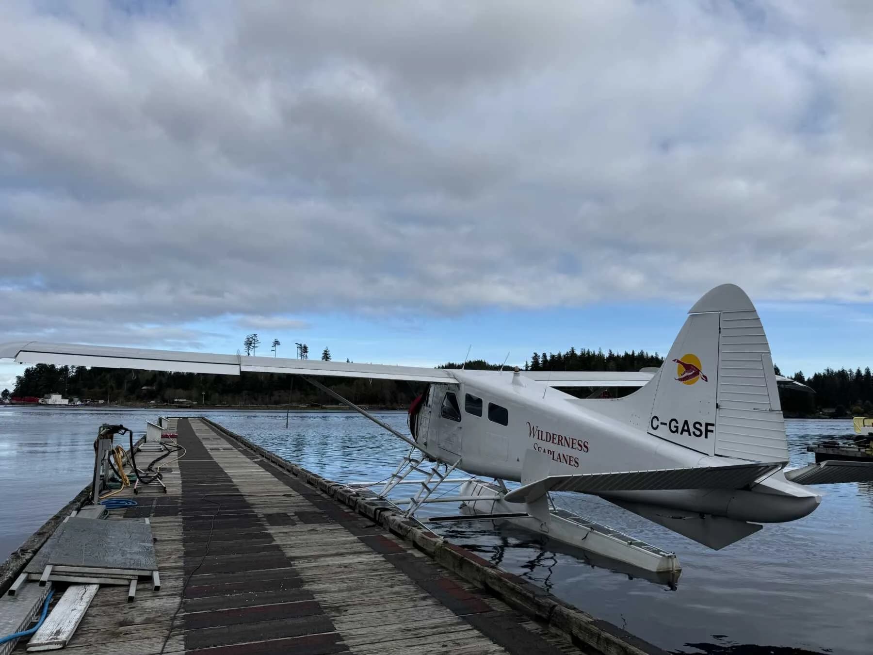 Side view of a de Havilland Beaver floatplane on a dock, showing the tail number C-GASF.