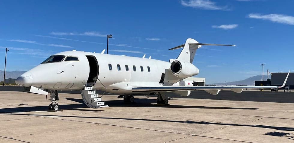 A white Bombardier Challenger 300 aircraft parked on the tarmac with the entry stairs extended.