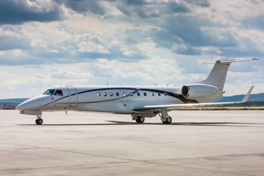 An Embraer Legacy 650 stands on the tarmac under a cloudy sky.